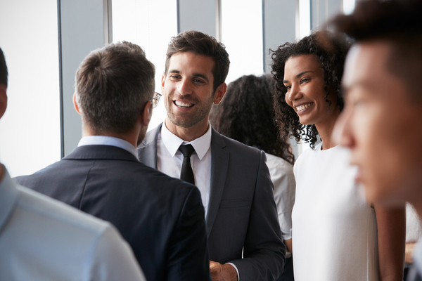 3 people in suits smile and talk in a crowd