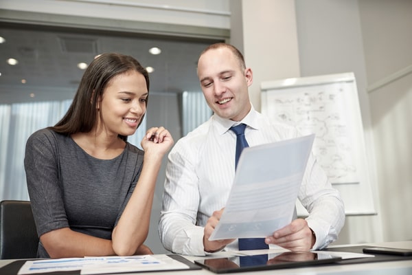 man shows woman information on a paper at a desk