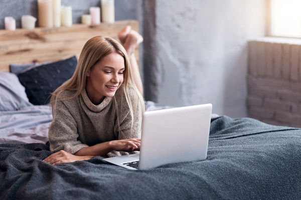 woman lays on her bed and uses her laptop