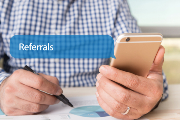 man writing and getting a text that says "referrals" on his cell phone
