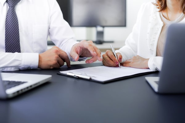 man and woman at table gesture at and write on clipboard