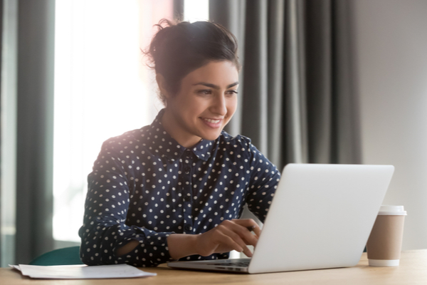 woman in blue and white shirt works at laptop and smiles