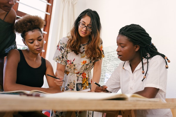 4 women look at a book on a table