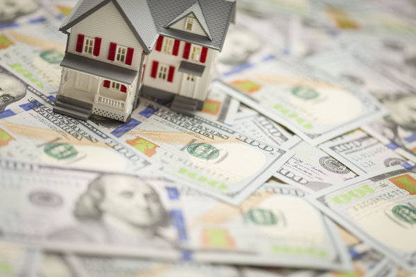 a miniature house sits on dollar bills