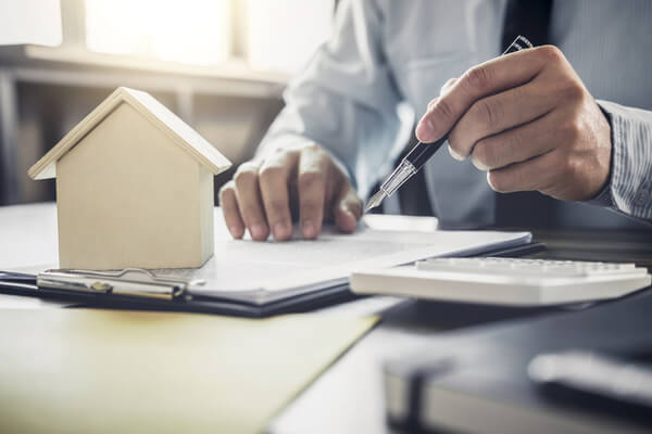 person with pen points to clipboard with model house on it