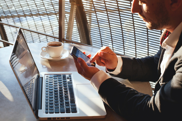 man using his phone at a laptop